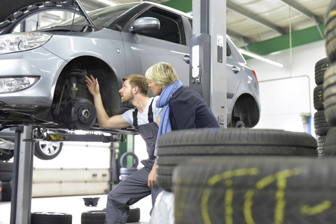 Car mechanic with client in workshop at car stock photo