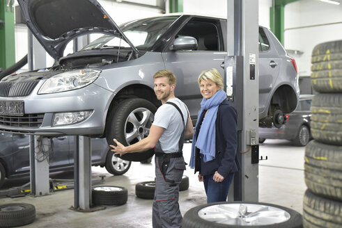 Porträt eines lächelnden Automechanikers mit einem Kunden in der Werkstatt am Auto - LYF00701