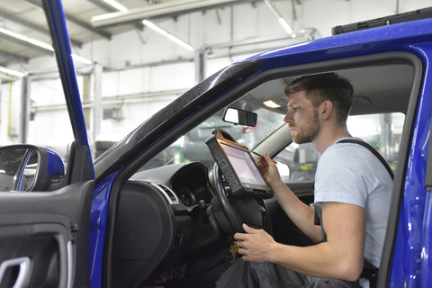 Automechaniker in einer Werkstatt mit Diagnosecomputer im Auto, lizenzfreies Stockfoto