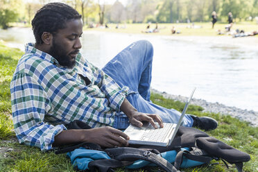 Man on a meadow using laptop - TCF05405