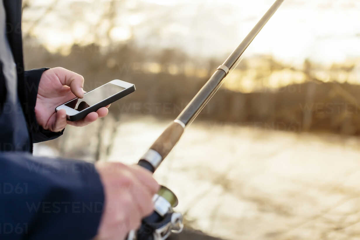 Man fishing looking at cell phone stock photo