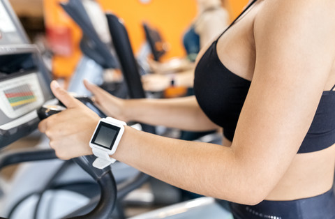 Frau im Fitnessstudio mit Smartwatch auf einem Ellipsentrainer, lizenzfreies Stockfoto