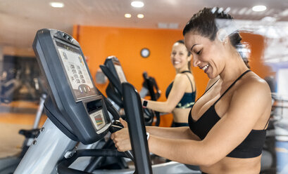 Zwei Frauen trainieren im Fitnessstudio auf einem Ellipsentrainer - MGOF03270