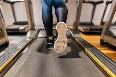 Nahaufnahme einer Frau, die in einem Fitnessstudio auf einem Laufband trainiert - MGOF03275