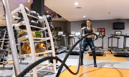 Junge Frau macht Battle-Rope-Übung im Fitnessstudio - MGOF03282