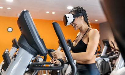 Frau mit VR-Brille auf einem elliptischen Trainingsgerät im Fitnessstudio - MGOF03293