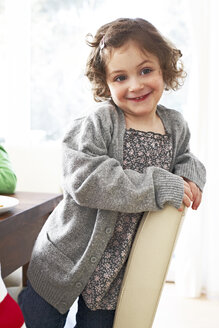 Porträt eines lächelnden kleinen Mädchens, das zu Hause auf einem Stuhl kniet - FSF00833