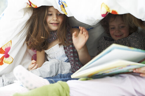 Drei kleine Kinder mit Buch zusammen unter der Bettdecke - FSF00845