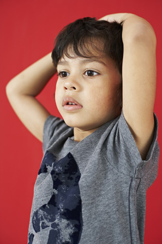 Porträt eines kleinen Jungen mit Händen auf dem Kopf vor einem roten Hintergrund, lizenzfreies Stockfoto