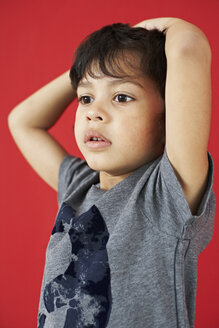 Porträt eines kleinen Jungen mit Händen auf dem Kopf vor einem roten Hintergrund - FSF00866