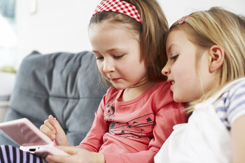 Zwei kleine Mädchen sitzen nebeneinander auf der Couch und schauen auf ihr Handy - FSF00871