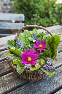 Essbare Blumen, Blätter und Kräuter in einem Weidenkorb auf dem Gartentisch - GWF05192