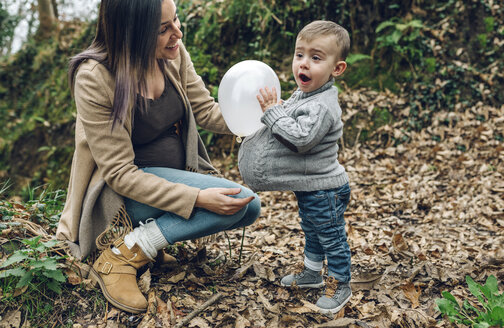 Happy pregnant mother and little boy having fun with a balloon in forest - DAPF00728