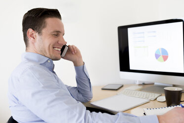 Smiling businessman on the phone at desk - FMOF00272