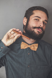 Man combing his beard with a wooden brush, wearing denim shirt and cork bow tie - RTBF00832