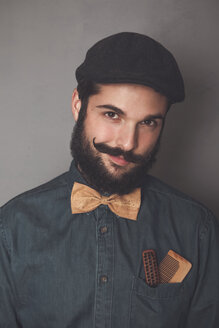 Portrait of bearded man wearing cap, denim shirt, cork bow tie, wearing wooden combs for beard and mustache in his pocket - RTBF00839