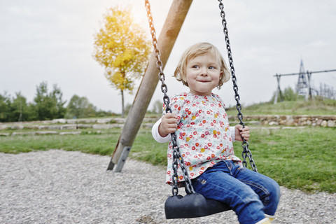 Lächelndes Mädchen auf der Schaukel auf dem Spielplatz, lizenzfreies Stockfoto