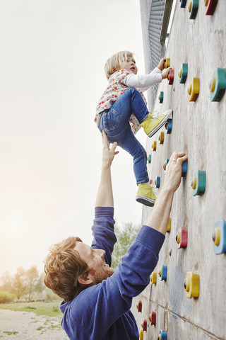 Girl climbing on a wall supported by father stock photo