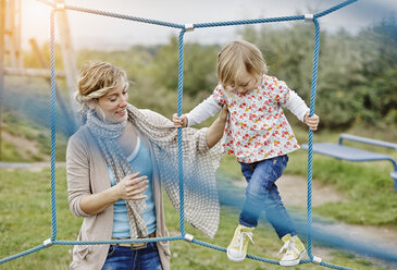 Mädchen auf Spielplatz im Kletternetz, gestützt von der Mutter - RORF00858