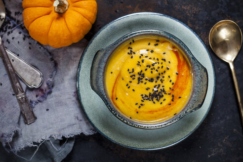 Schale mit Kürbiscremesuppe mit Schwarzkümmel bestreut neben Kürbissen - SBDF03202