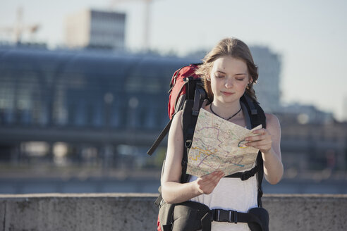 Germany, Berlin, Young woman with backpack looking at map - MVCF00170