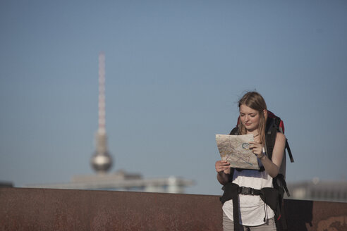 Germany, Berlin, Young woman with backpack looking at map - MVCF00171