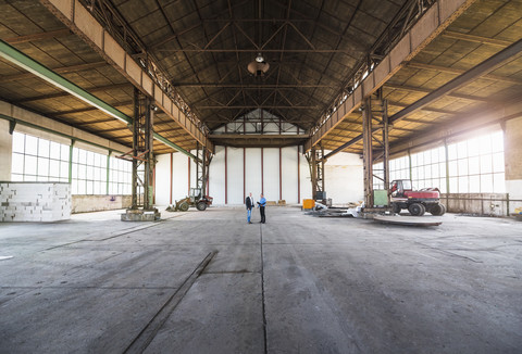 Zwei Geschäftsleute mit Dokumenten im Gespräch in einer alten Industriehalle, lizenzfreies Stockfoto