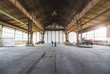 Zwei Geschäftsleute mit Dokumenten im Gespräch in einer alten Industriehalle - DIGF02412