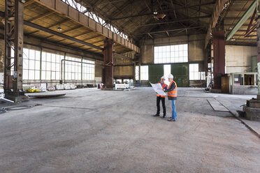 Zwei Männer mit Plan und Sicherheitswesten im Gespräch in einer alten Industriehalle - DIGF02416