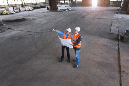 Zwei Männer mit Plan und Sicherheitswesten im Gespräch in einer alten Industriehalle - DIGF02417