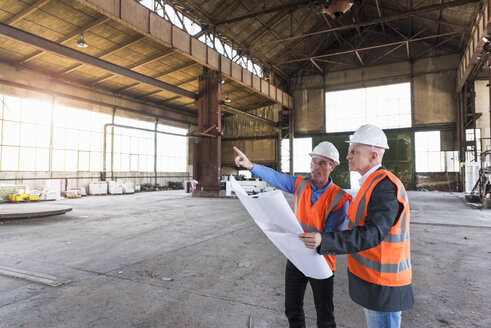 Zwei Männer mit Plan und Sicherheitswesten im Gespräch in einer alten Industriehalle - DIGF02418