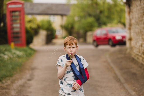 Boy with a broken arm blowing dandelion seeds - NMSF00075