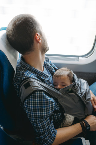 Vater im Zug, der sein schlafendes Baby in einer Babytrage hält, lizenzfreies Stockfoto