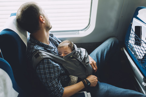 Father on the train holding his sleeping baby in a baby carrier stock photo