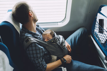 Vater im Zug, der sein schlafendes Baby in einer Babytrage hält - GEMF01604