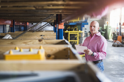 Mann mit Tablet in einer Industriehalle, der sich Regale ansieht - DIGF02434