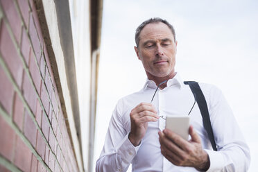 Businessman at brick wall using cell phone - DIGF02444