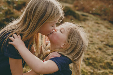 Two cute blond sisters kissing outdoors - NMSF00102