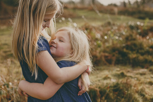 Two cute blond sisters cuddling outdoors - NMSF00103