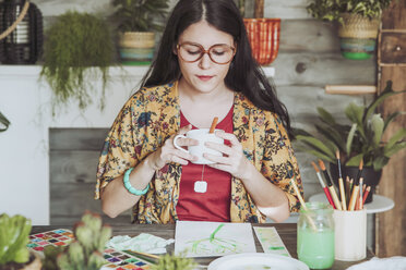 Young woan drinking tea and lookig at her paintings of plants - RTBF00851