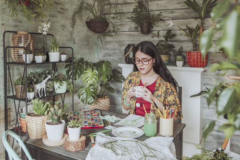 Junge Frau, die Tee trinkt und sich ihre Pflanzenbilder ansieht - RTBF00852
