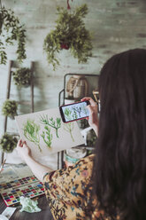Junge Frau, die mit ihrem Smartphone Bilder von bemalten Pflanzen macht - RTBF00862