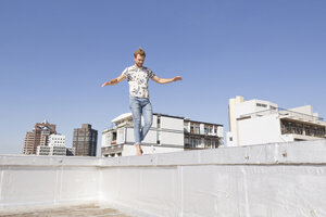 Barfüßiger Mann balanciert auf der Brüstung einer Dachterrasse - WESTF23068