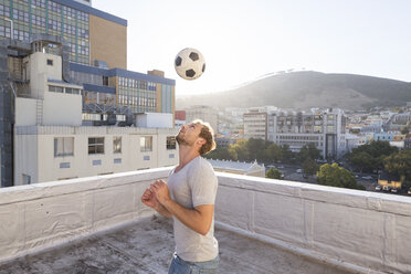 Young man playing football on rooftop terrace - WESTF23069