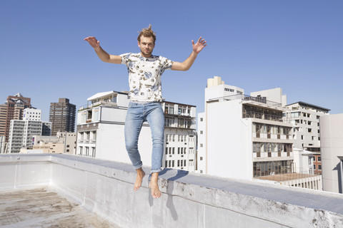 Barfüßiger Mann springt von der Brüstung einer Dachterrasse, lizenzfreies Stockfoto