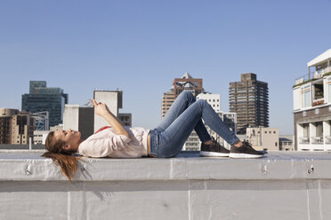 Young woman lying on balustrade of a rooftop terrace, using smart phone - WESTF23081