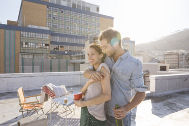 Young couple celebrating on a rooftop terrace, embracing at sunset - WESTF23112