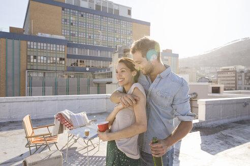 Junges Paar, das auf einer Dachterrasse feiert und sich bei Sonnenuntergang umarmt - WESTF23112