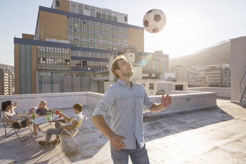 Friends meeting on rooftop terrace in summer, playing football - WESTF23122