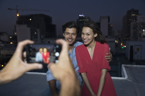 Junger Mann fotografiert ein Paar auf einer Dachterrassenparty, lizenzfreies Stockfoto